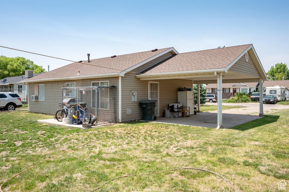 Back of property with roof with shingles, a yard, and a carport