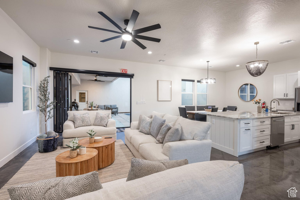 Living room featuring a ceiling fan, recessed lighting, a chandelier, and finished concrete floors
