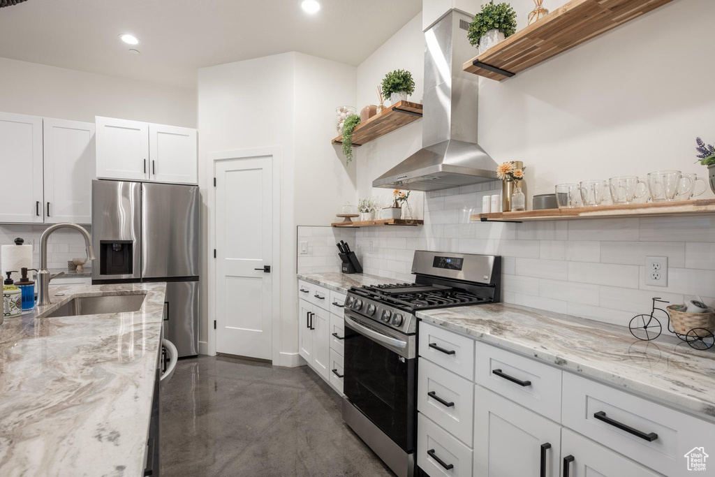 Kitchen featuring stainless steel appliances, open shelves, wall chimney exhaust hood, concrete floors, and decorative backsplash