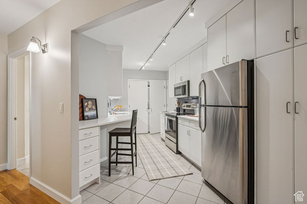 Kitchen featuring stainless steel appliances, a kitchen breakfast bar, light countertops, rail lighting, and white cabinetry