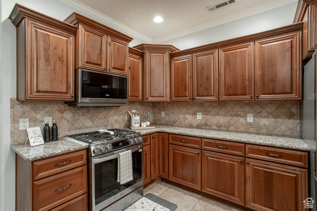 Kitchen featuring appliances with stainless steel finishes, crown molding, light tile patterned floors, and brown cabinetry