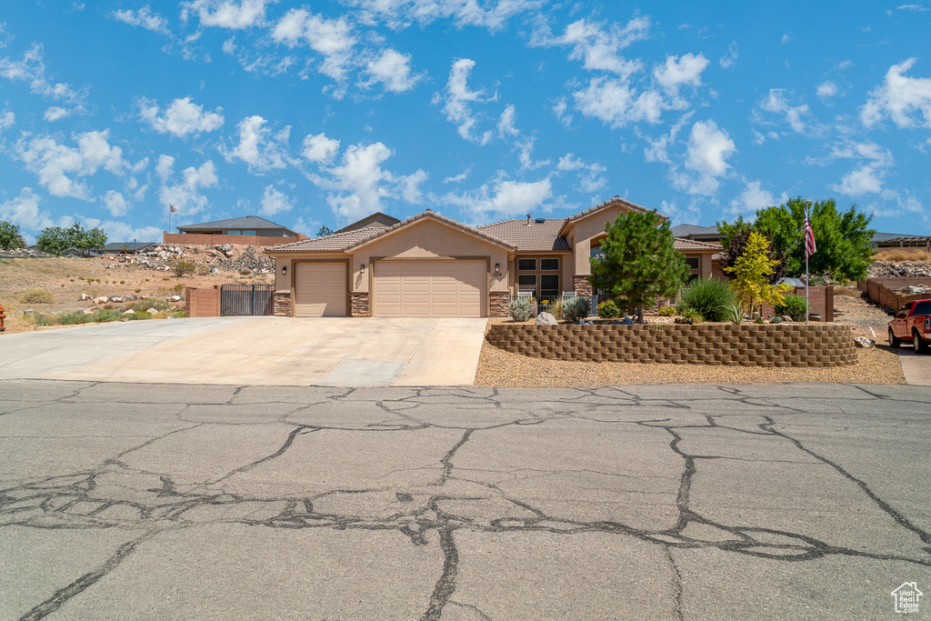 View of front facade with stucco siding, a garage, driveway, stone siding, and a tile roof