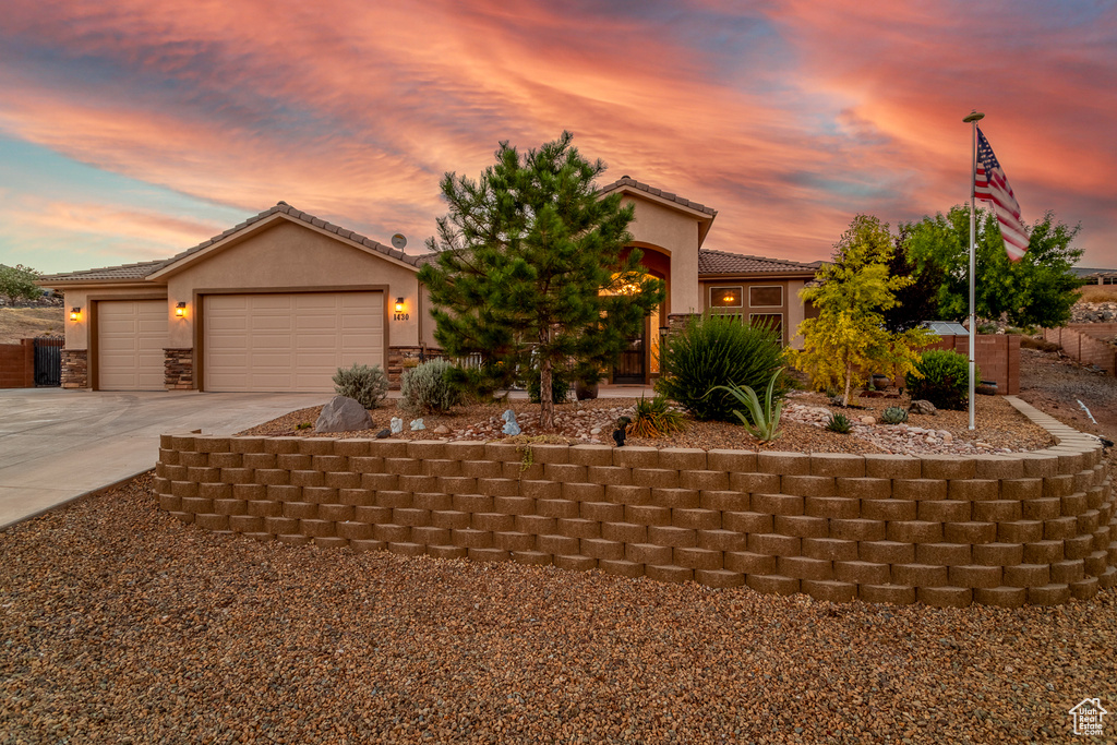 View of front of property with concrete driveway, stucco siding, a tiled roof, an attached garage, and stone siding