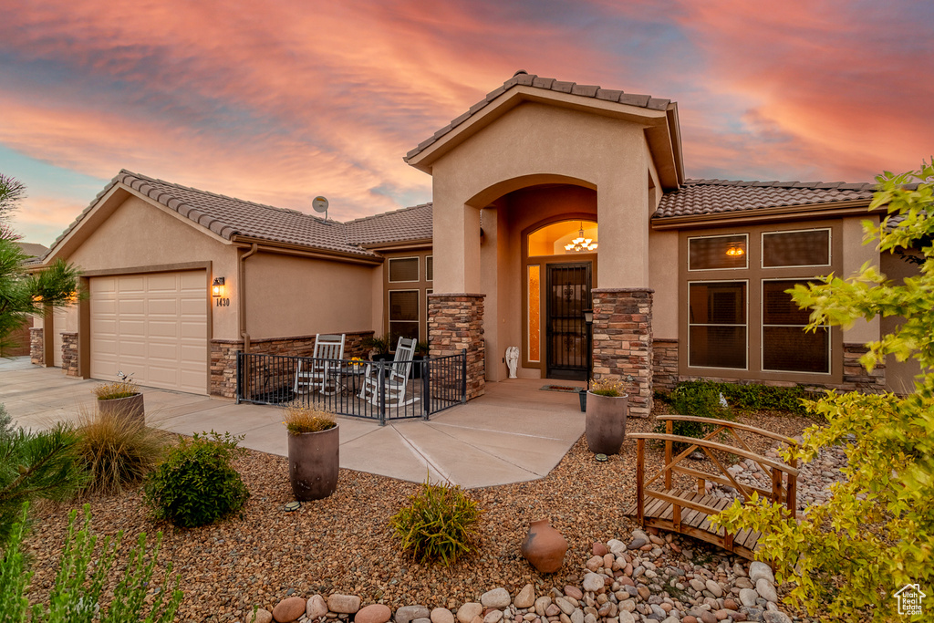 Mediterranean / spanish-style house with stone siding, a tiled roof, an attached garage, and stucco siding
