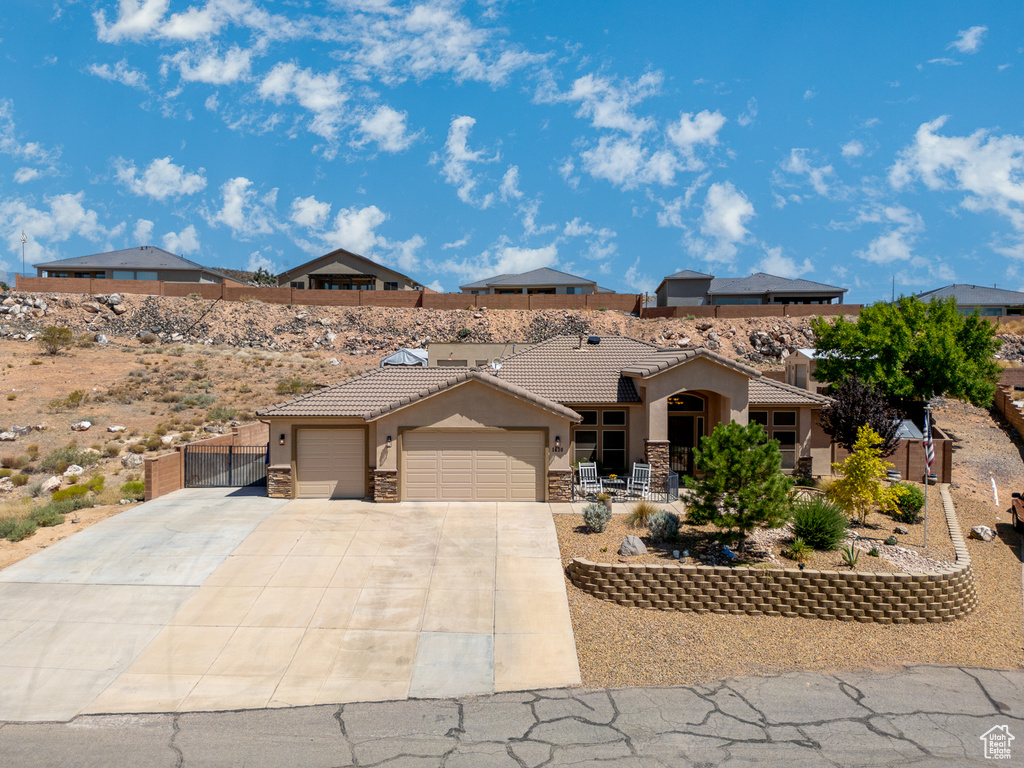 View of front facade featuring stucco siding, an attached garage, a tile roof, driveway, and stone siding