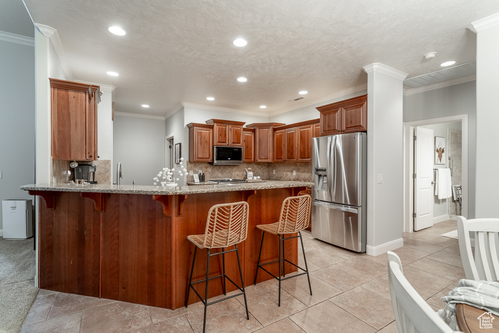 Kitchen with stainless steel appliances, a peninsula, light stone countertops, decorative backsplash, and a kitchen bar