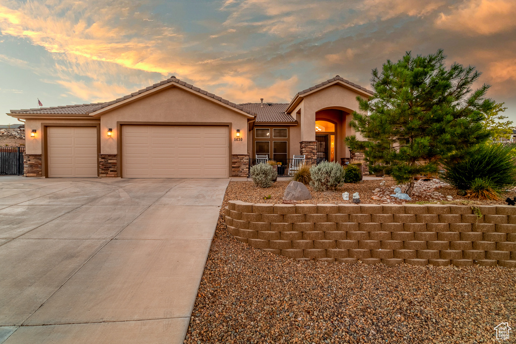 View of front facade with stone siding, stucco siding, an attached garage, driveway, and a tile roof
