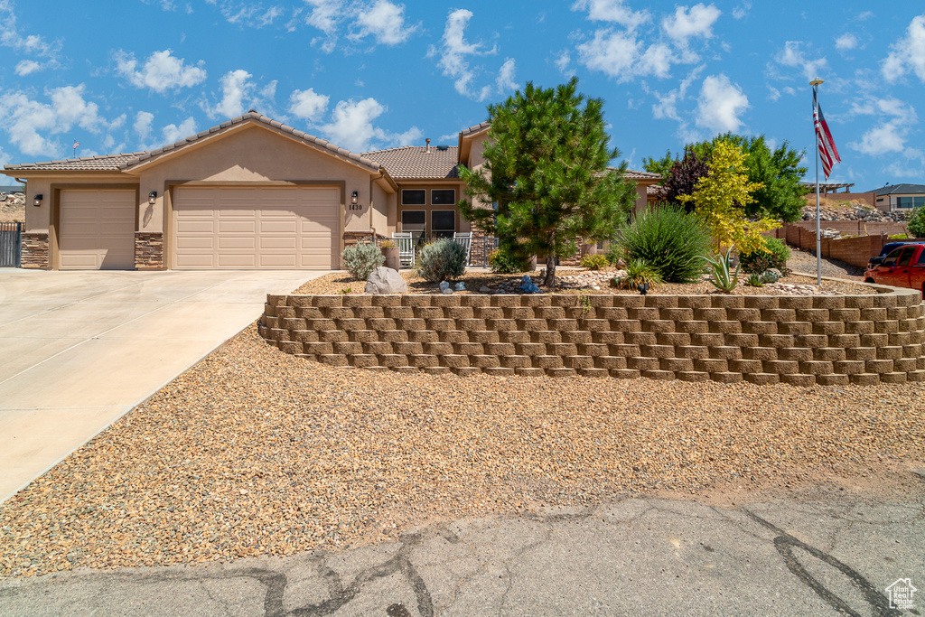 View of front of property with stucco siding, a garage, driveway, a tile roof, and stone siding