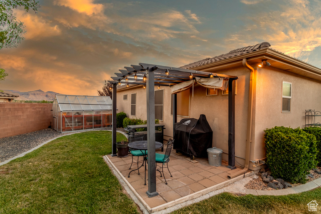 Patio terrace at dusk featuring a greenhouse, a grill, a fenced backyard, an outdoor structure, and a patio area