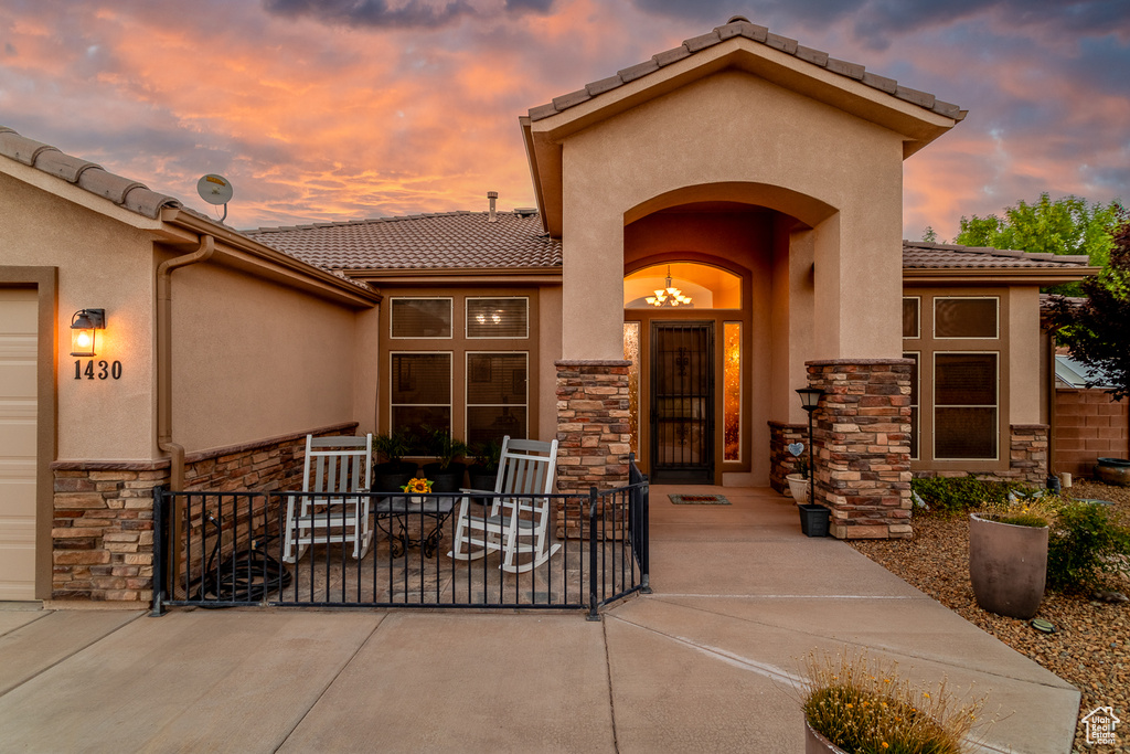 Entrance to property featuring stone siding, a tile roof, and stucco siding