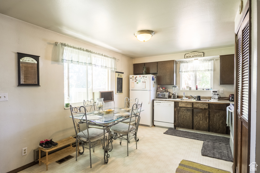 Kitchen featuring white appliances, dark brown cabinetry, light countertops, and light flooring
