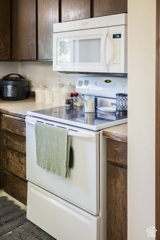 Kitchen featuring white appliances, dark brown cabinets, and light countertops
