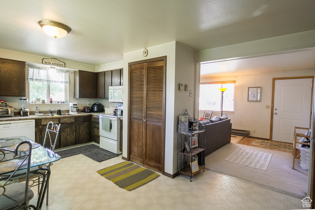 Kitchen with white appliances, dark brown cabinetry, light countertops, and a baseboard heating unit