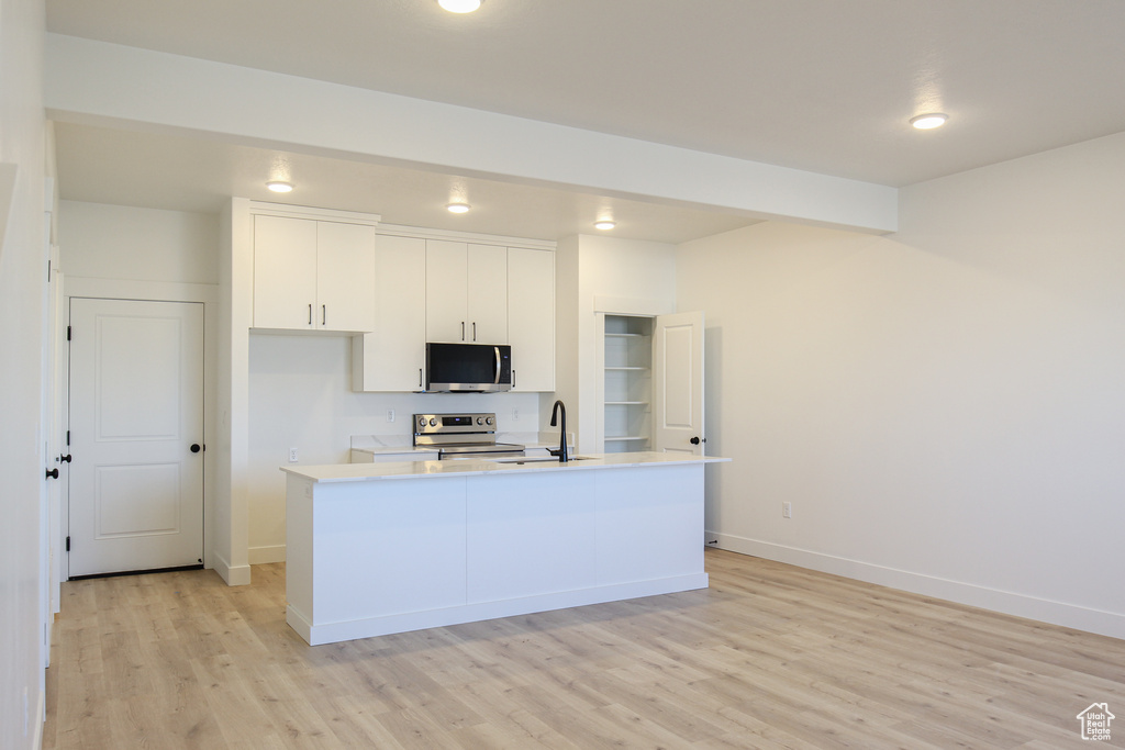 Kitchen featuring appliances with stainless steel finishes, light wood-type flooring, white cabinetry, light countertops, and a center island with sink