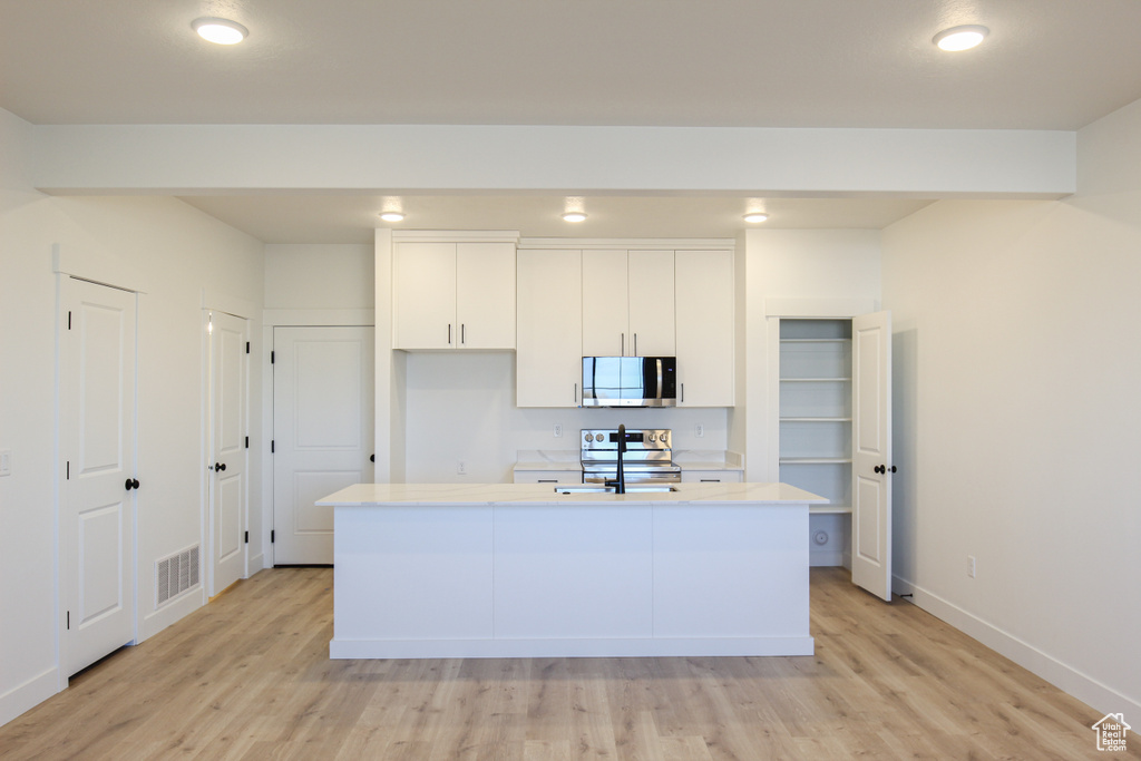 Kitchen with appliances with stainless steel finishes, light wood-type flooring, light countertops, white cabinetry, and a kitchen island with sink
