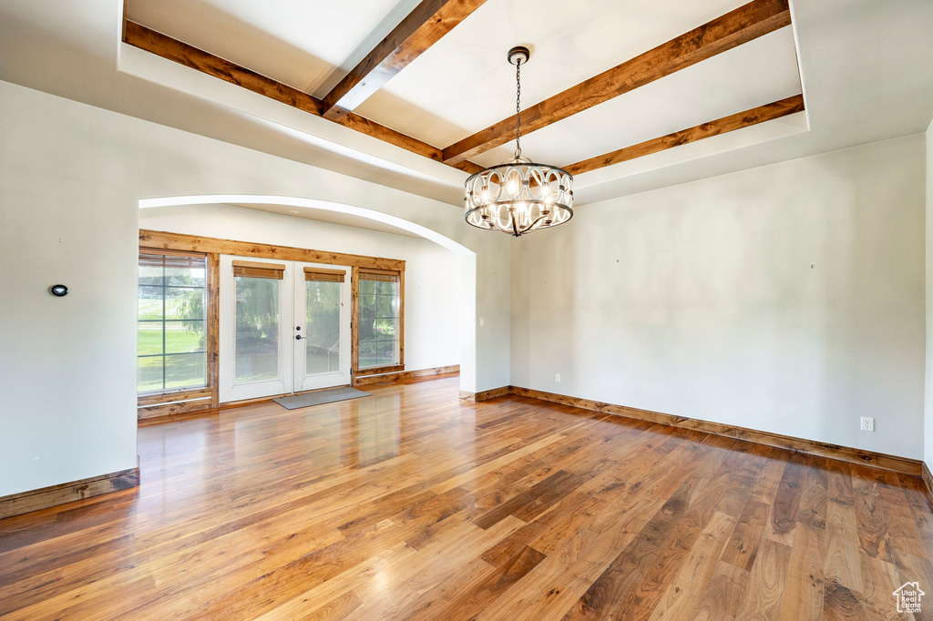 Spare room featuring wood-type flooring, beam ceiling, a chandelier, french doors, and arched walkways