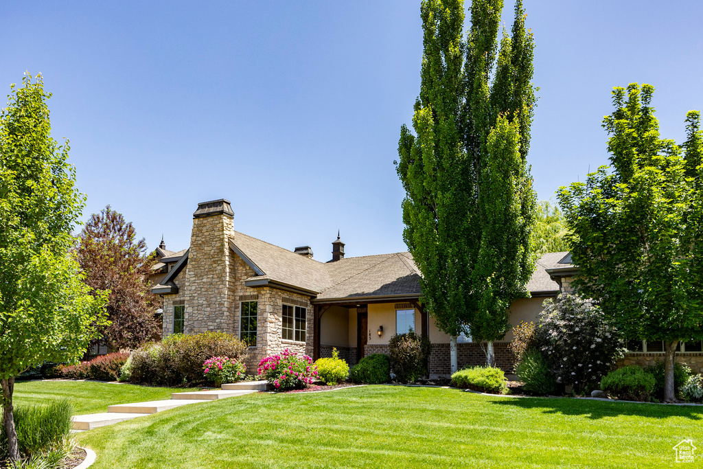 View of front of home featuring stone siding, a front lawn, and a chimney