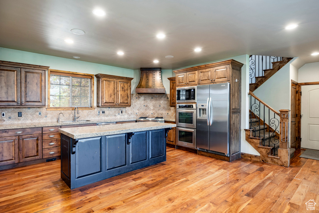 Kitchen featuring appliances with stainless steel finishes, custom exhaust hood, a center island, light wood-style flooring, and recessed lighting