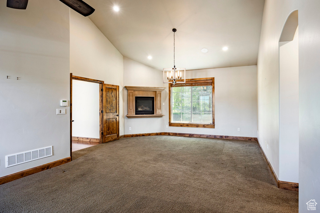 Carpeted spare room with recessed lighting, a chandelier, high vaulted ceiling, and a glass covered fireplace