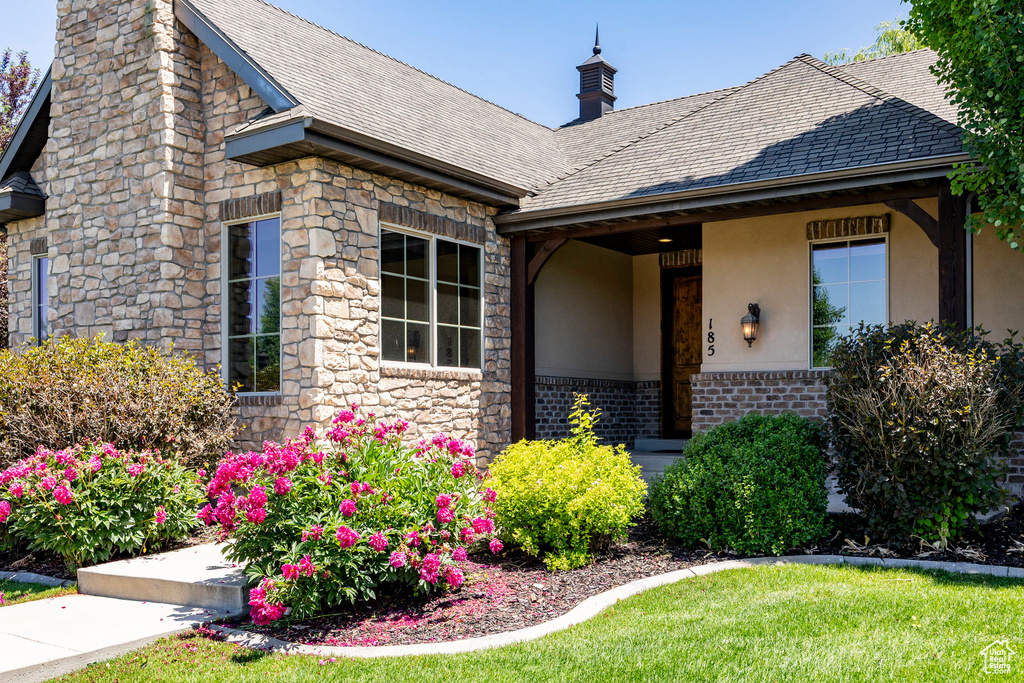 View of front facade featuring a chimney, stucco siding, a front lawn, stone siding, and roof with shingles