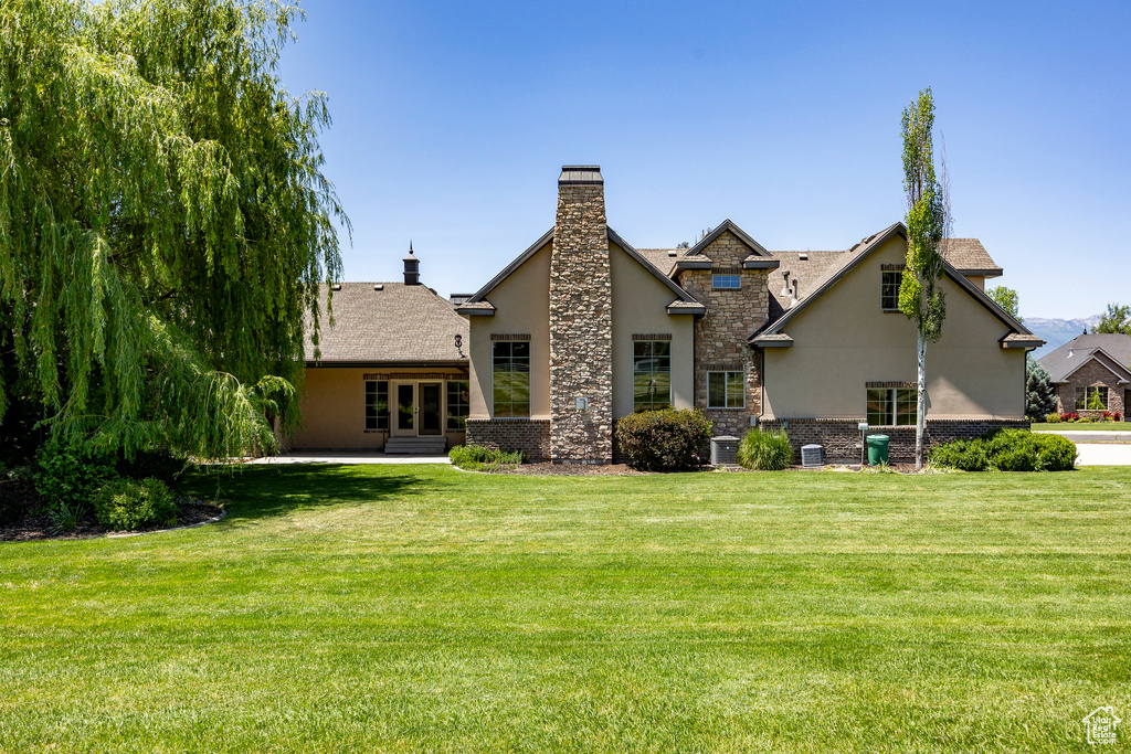 Rear view of property featuring stucco siding, a chimney, french doors, a lawn, and stone siding