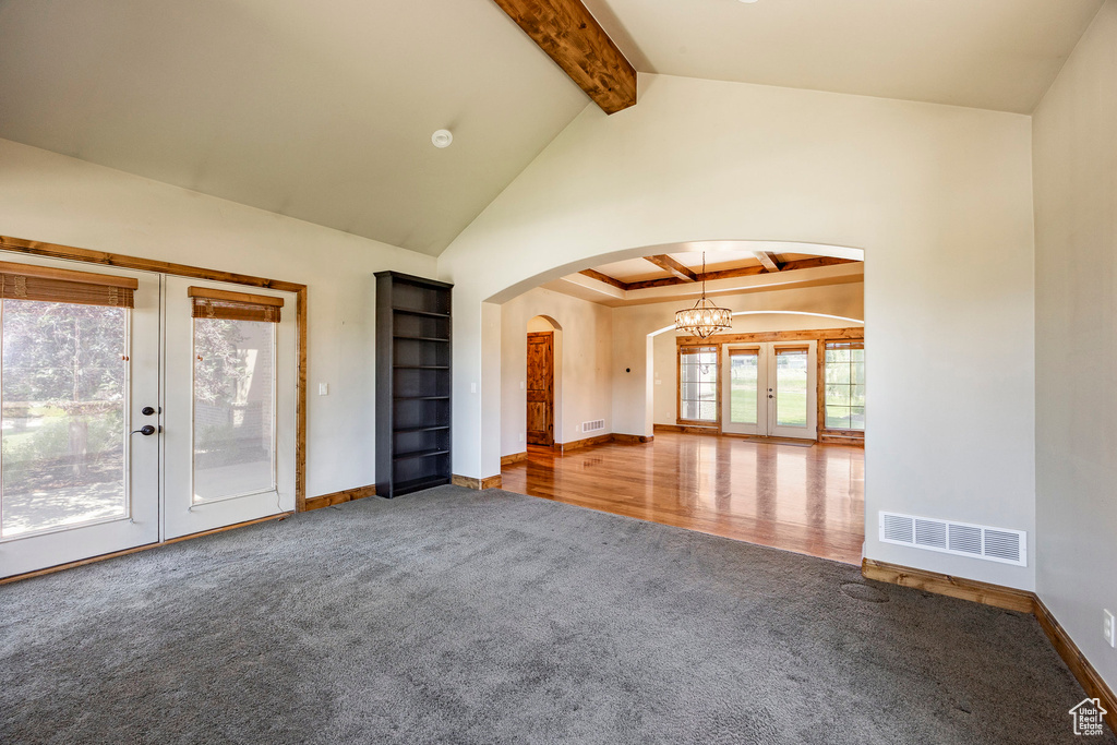 Unfurnished living room with carpet floors, french doors, arched walkways, beamed ceiling, and a chandelier