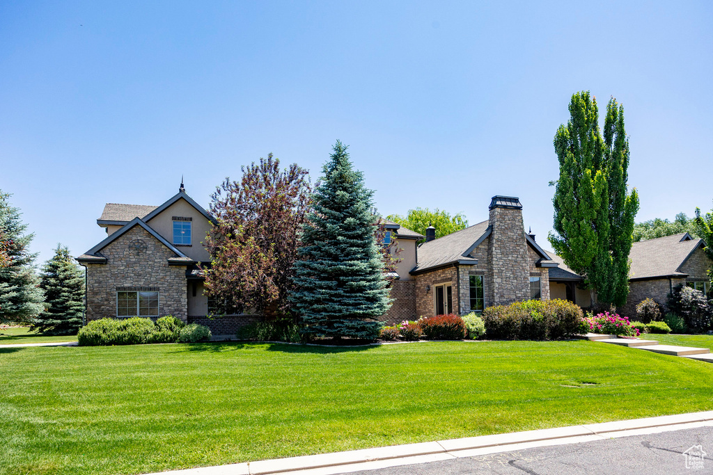 View of front of home with stone siding, a front yard, and a chimney