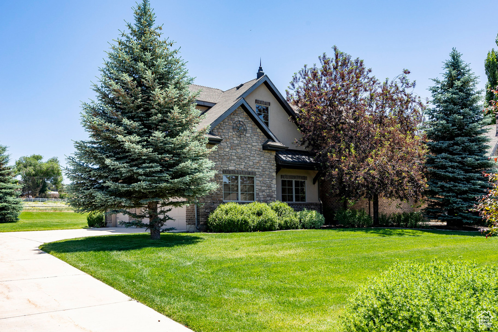 View of front of home with stone siding, concrete driveway, a front yard, a garage, and stucco siding