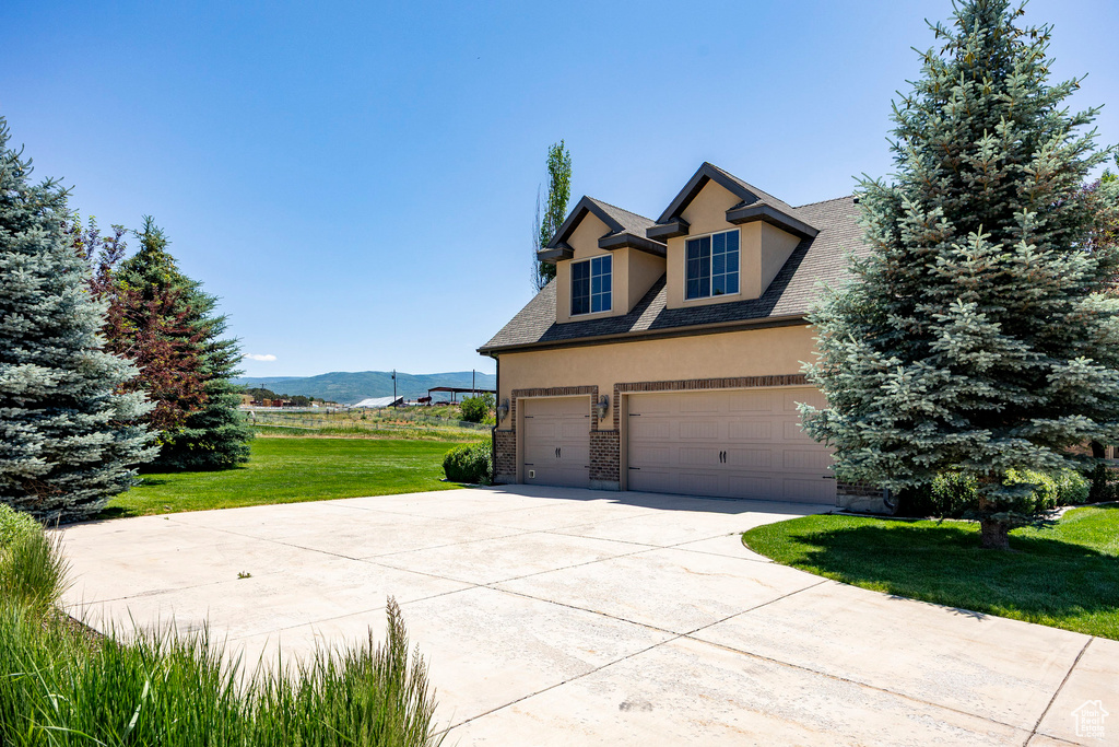 View of front of home with stucco siding, driveway, a front yard, a garage, and a mountain view