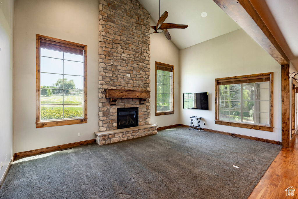 Unfurnished living room featuring healthy amount of natural light, high vaulted ceiling, a ceiling fan, a stone fireplace, and wood finished floors