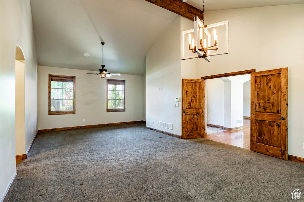 Carpeted empty room with high vaulted ceiling, arched walkways, beam ceiling, ceiling fan, and a chandelier