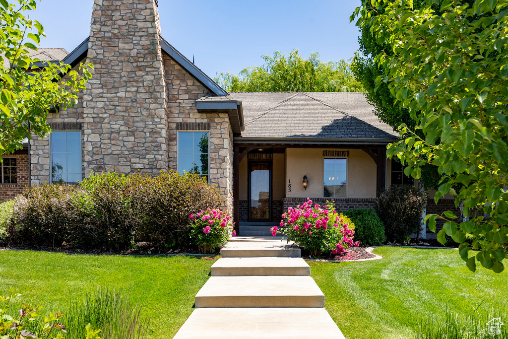 View of front of property featuring stone siding, a front lawn, roof with shingles, and a chimney