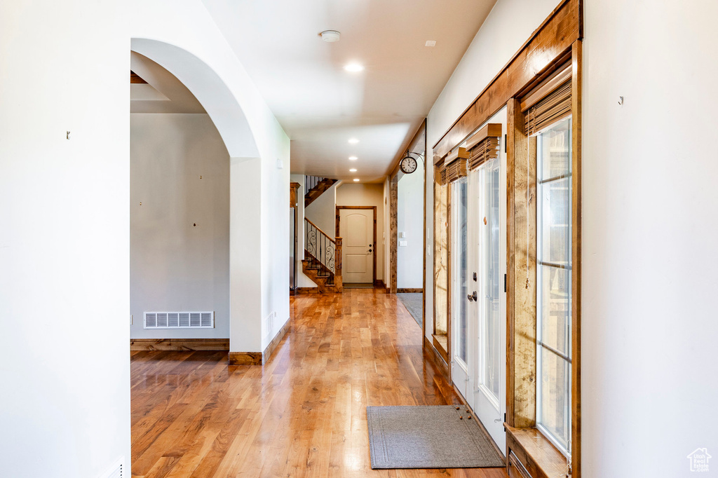 Hall with light wood finished floors, recessed lighting, arched walkways, and stairs