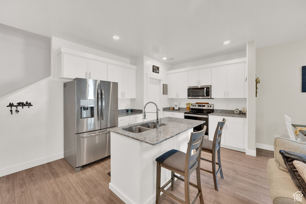 Kitchen with appliances with stainless steel finishes, light wood finished floors, a kitchen breakfast bar, recessed lighting, and light stone countertops