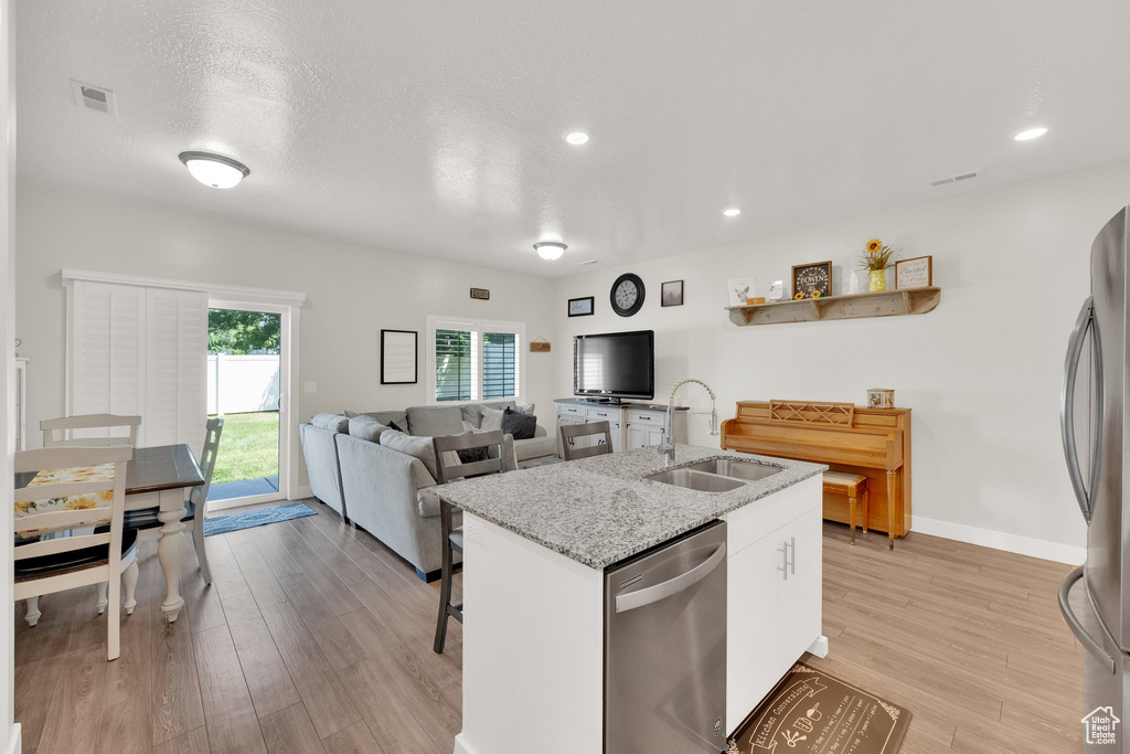 Kitchen featuring stainless steel appliances, light wood-style flooring, white cabinetry, an island with sink, and recessed lighting