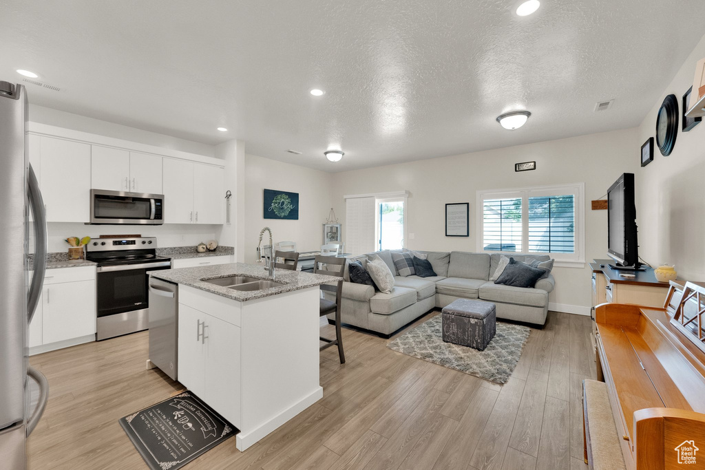 Kitchen with stainless steel appliances, light wood finished floors, open floor plan, a kitchen island with sink, and white cabinetry