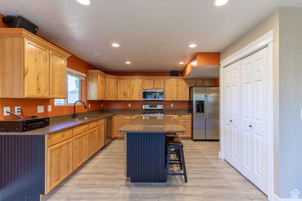 Kitchen featuring appliances with stainless steel finishes, recessed lighting, a breakfast bar, a kitchen island, and light wood-style flooring