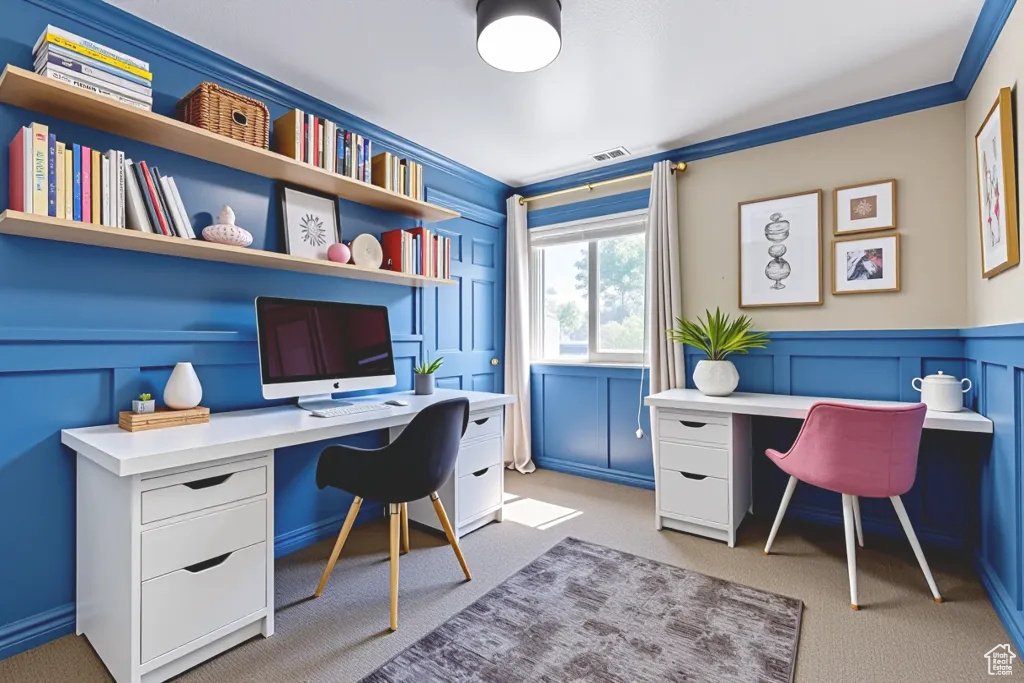 Home office featuring built in desk, light colored carpet, a decorative wall, ornamental molding, and wainscoting