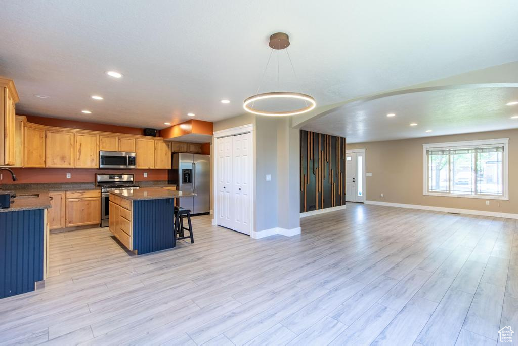 Kitchen featuring appliances with stainless steel finishes, open floor plan, a breakfast bar, recessed lighting, and light wood-type flooring