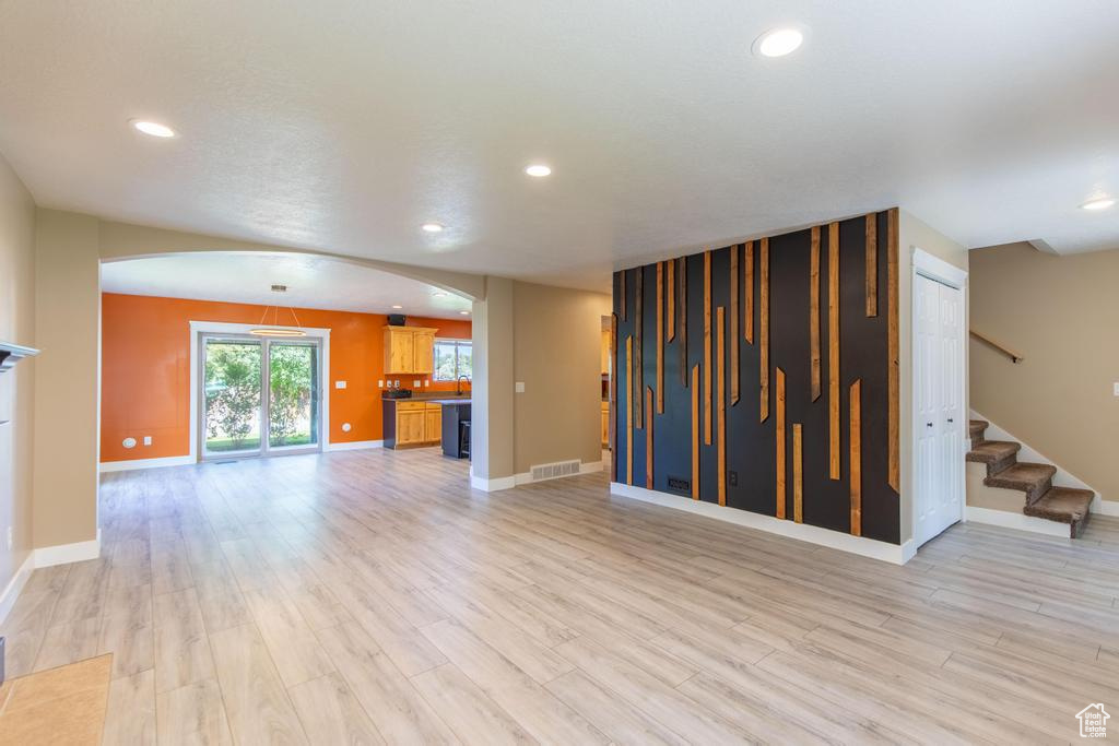 Unfurnished living room featuring arched walkways, light wood finished floors, recessed lighting, and stairs