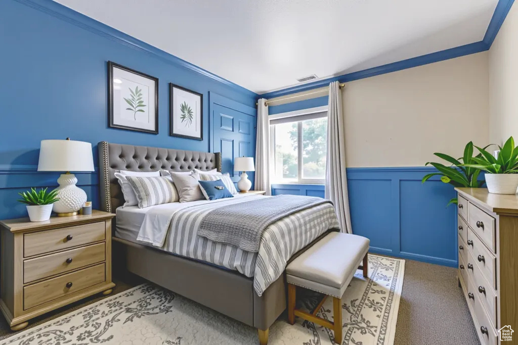 Bedroom with a decorative wall, wainscoting, ornamental molding, and light colored carpet