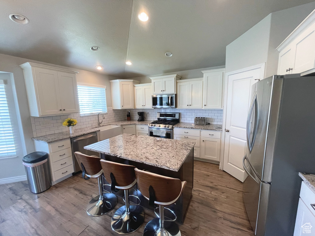 Kitchen featuring appliances with stainless steel finishes, wood finished floors, tasteful backsplash, a kitchen island, and recessed lighting