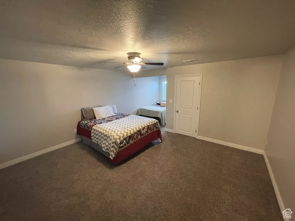 Bedroom featuring dark colored carpet, a textured ceiling, and a ceiling fan