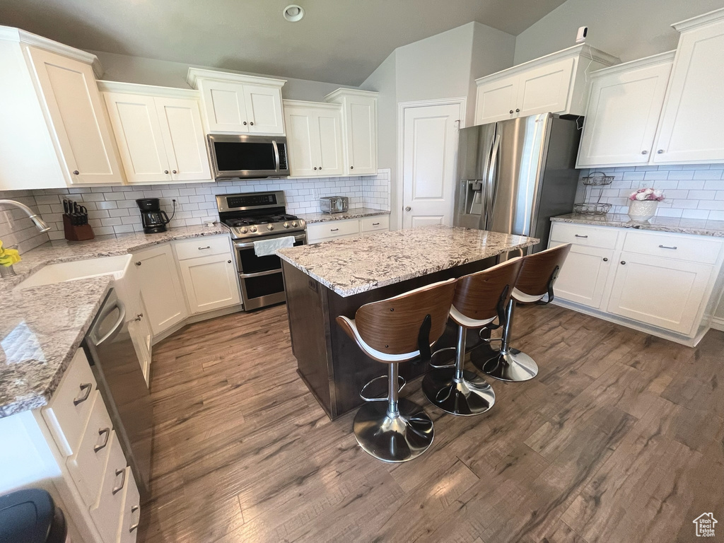 Kitchen with stainless steel appliances, decorative backsplash, white cabinetry, a kitchen island, and dark wood-type flooring