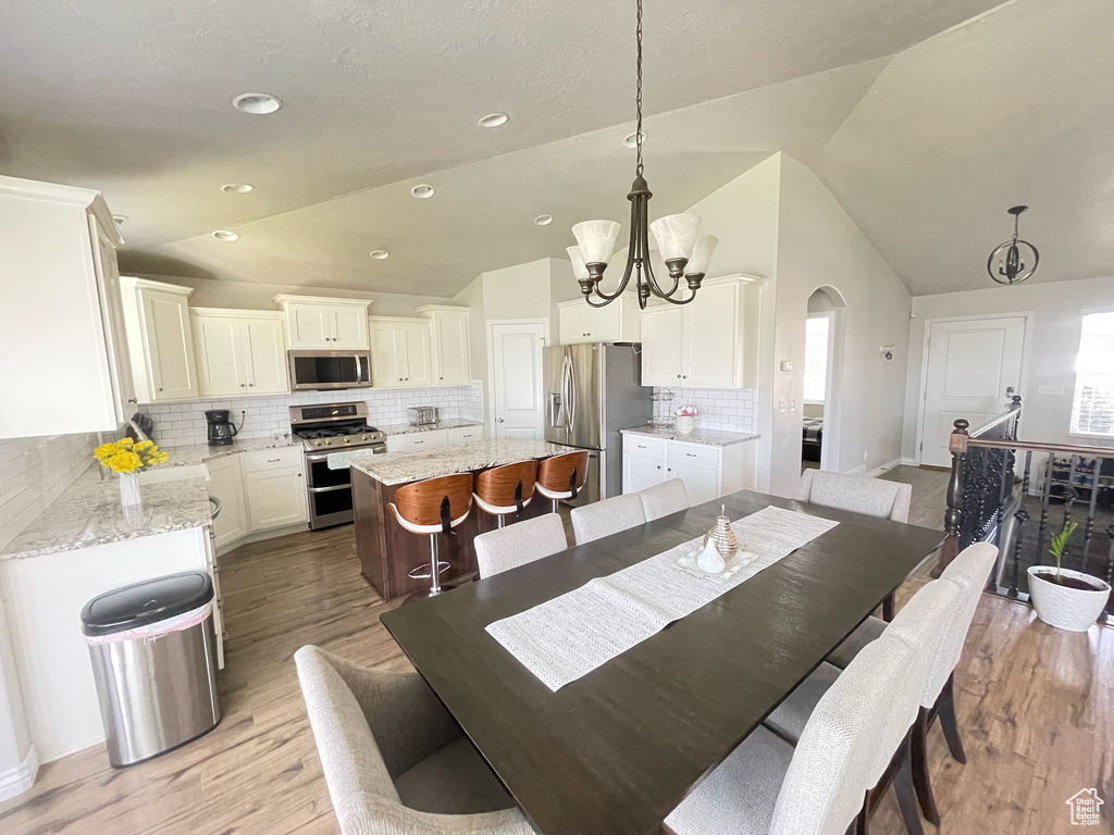 Dining room featuring lofted ceiling, a chandelier, arched walkways, and light wood-style floors