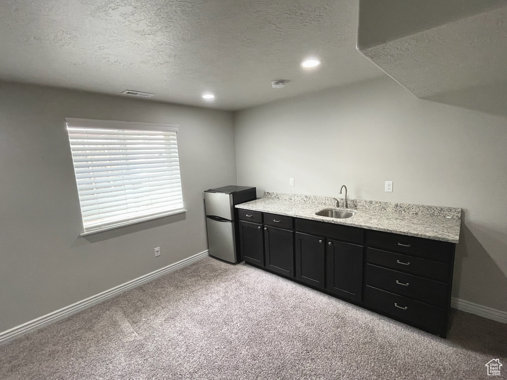 Bar area with freestanding refrigerator, a textured ceiling, light carpet, and recessed lighting