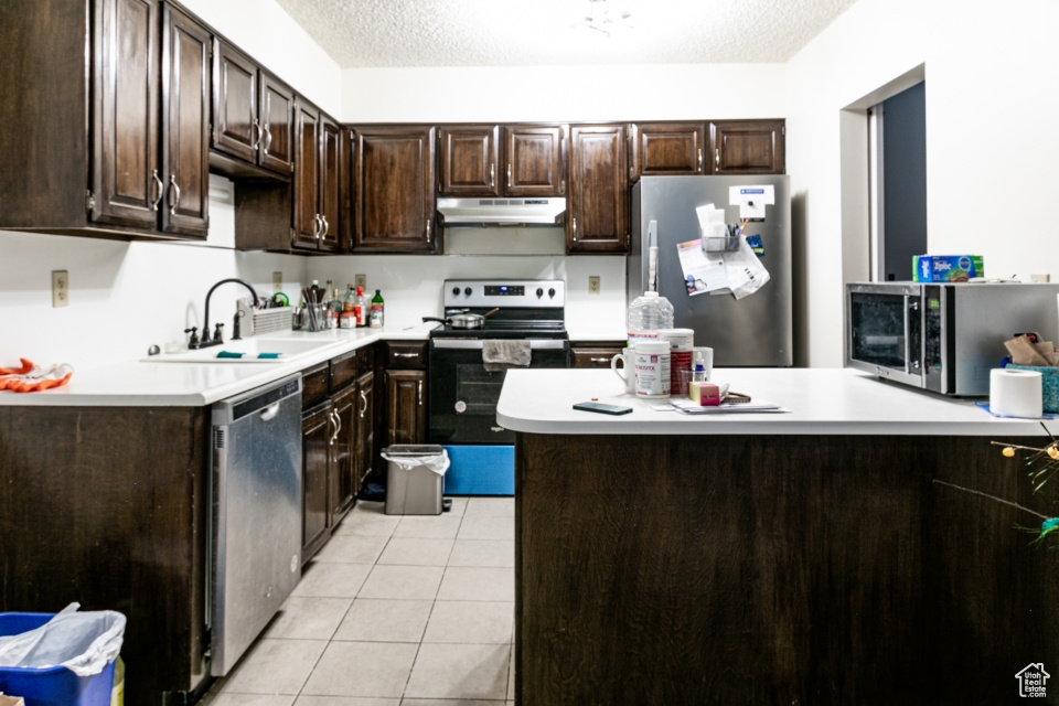 Kitchen featuring appliances with stainless steel finishes, under cabinet range hood, dark brown cabinets, light countertops, and light tile patterned flooring