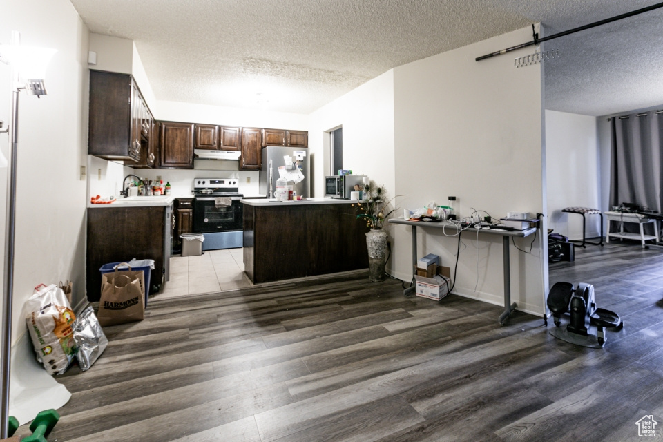 Kitchen with stainless steel appliances, light wood finished floors, a textured ceiling, under cabinet range hood, and dark brown cabinetry