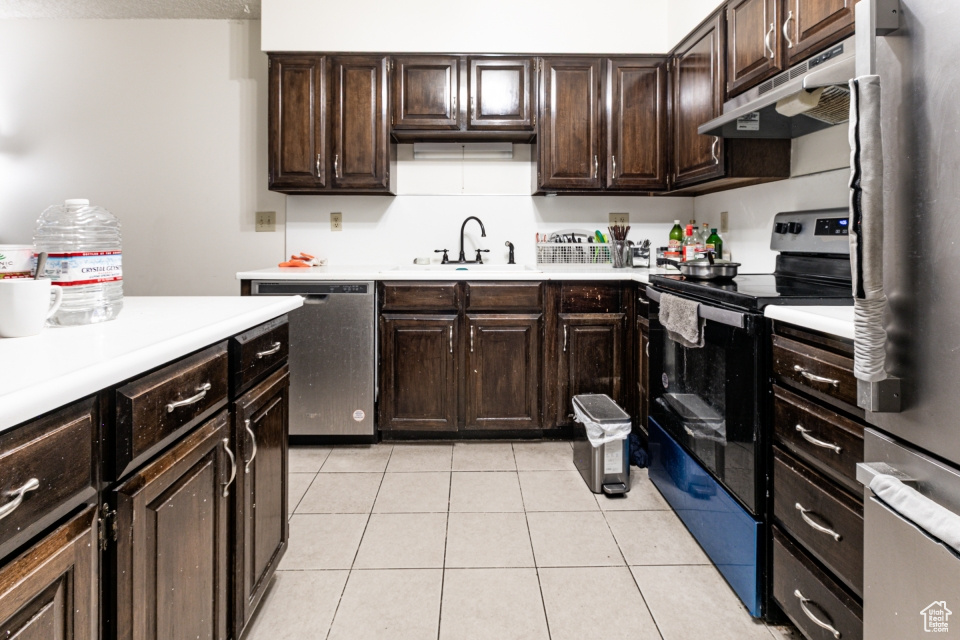 Kitchen with appliances with stainless steel finishes, under cabinet range hood, light countertops, and light tile patterned floors