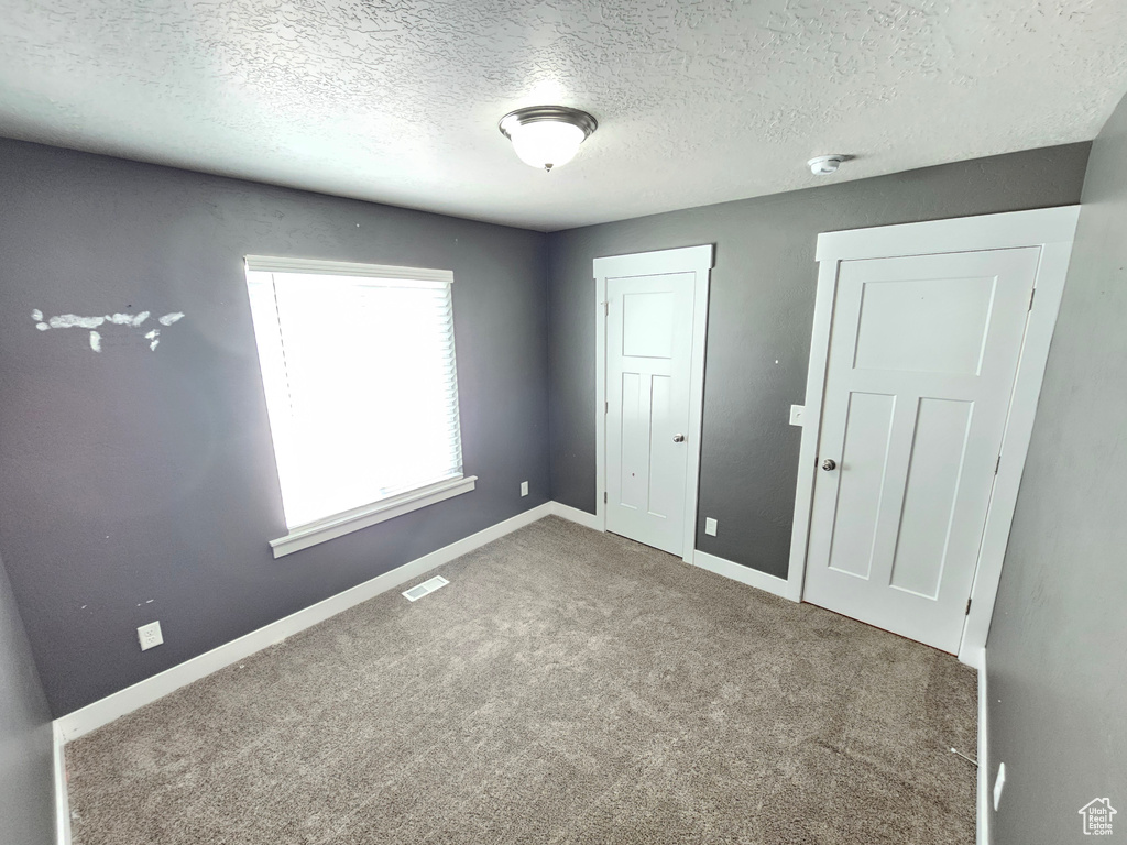 Unfurnished bedroom featuring a textured ceiling, carpet floors, and a closet